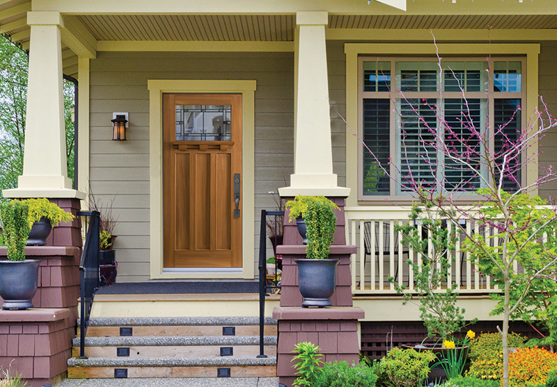 Craftsman-style fiberglass entry door installed on a classic front porch with warm wood tones and decorative glass