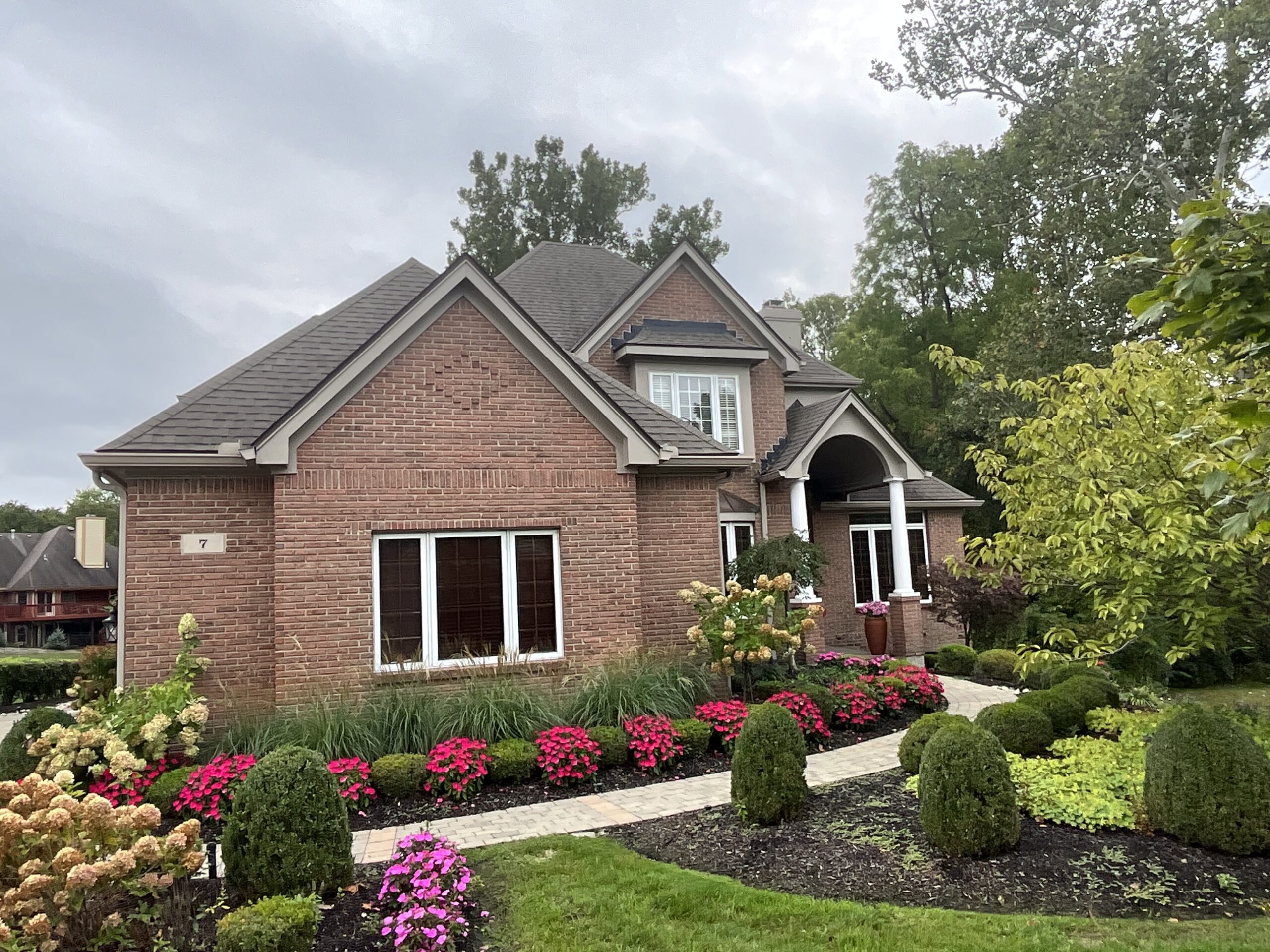 Top shingle colors example featuring rich brown GAF Timberline shingles on a luxurious two-story brick home with gable roof, beige siding, dark shutters, and arched windows, showcasing enhanced curb appeal and timeless elegance