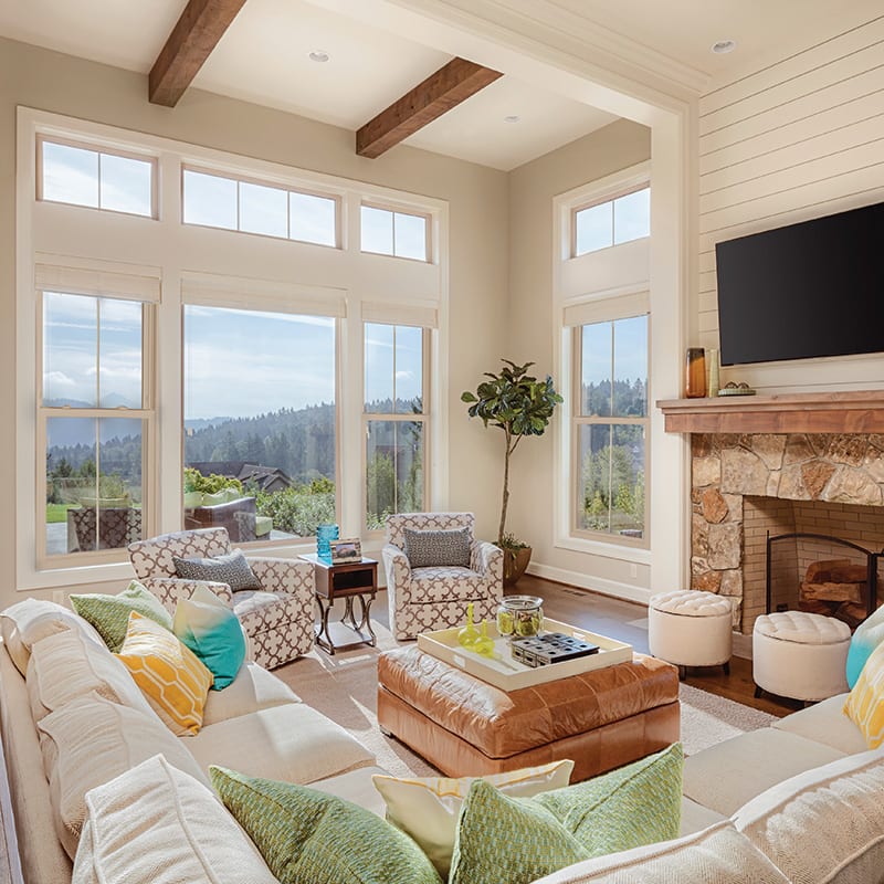 Bright living room with large sliding patio door and tall windows, wood ceiling beams, fireplace, and scenic outdoor views.