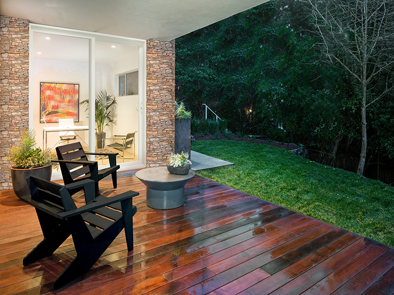 Outdoor deck with modern seating and a white sliding glass patio door set in a stone exterior wall, creating a seamless indoor-outdoor connection.